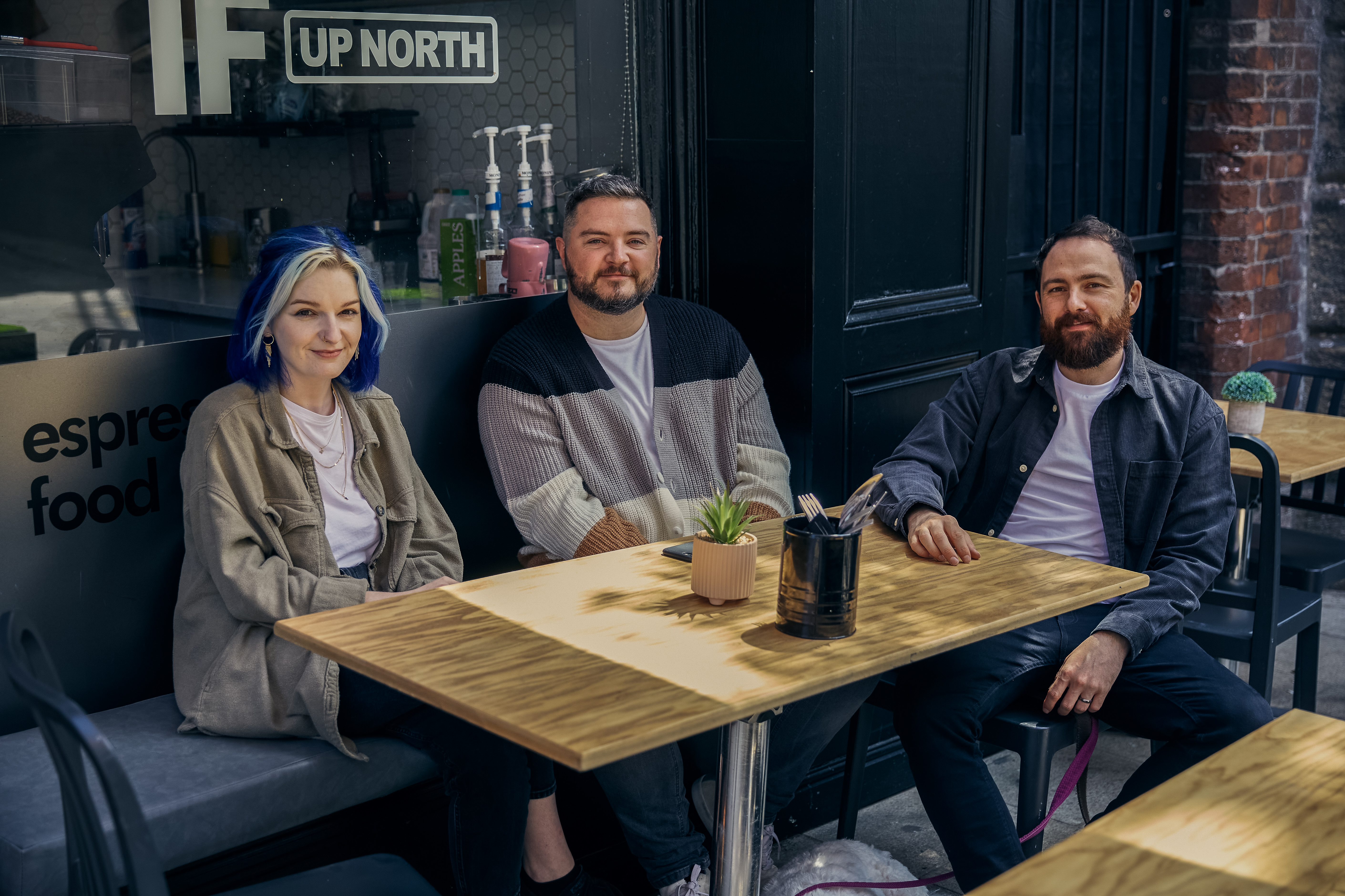 Three members of the Few and Far team are sat outside a Leeds Coffee shop