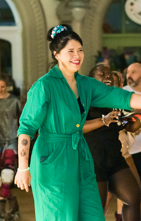 A lady in a green jump suit is shown smiling and wearing roller skates